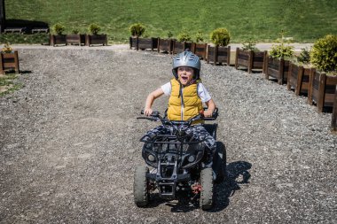 Little boy driving atv and having fun while riding on dirt road. 