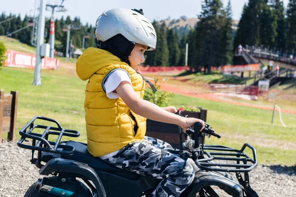 Side view of small boy driving quadbike in nature. 