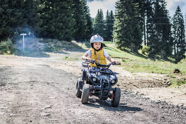 Little boy driving atv vehicle on off road track.