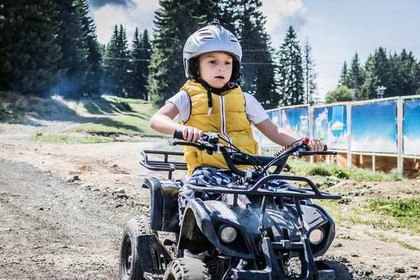 Small boy learning to drive four wheeled quad bike on mountain road.