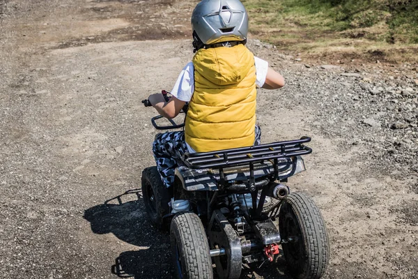 Rear view of small boy driving atv quad bike on off-road track. 