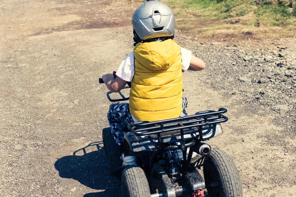 Rear view of boy on quadbike driving on dirt road in nature.