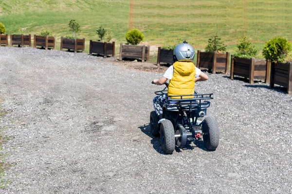 Rear view of kid driving on off road train on a quadbike. 