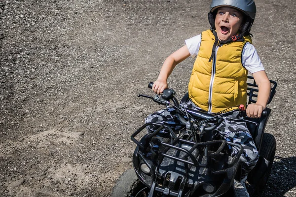 Small boy having fun while driving quad bike on dirt road.