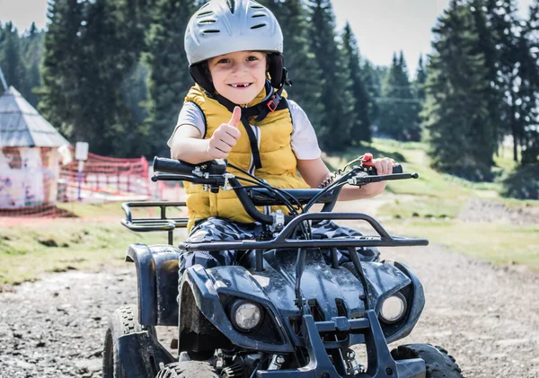 Happy kid showing thumbs up after riding quad bike in nature.