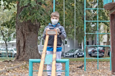 Small boy with protective face mask playing alone in the park.