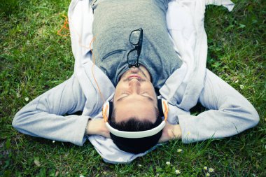 Carefree man with eyes closed relaxing on sprig grass and enjoying in music over headphones.