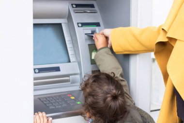 Mother and daughter withdrawing money form cash machine. Small girl assisting her mother with inserting credit card into ATM machine.
