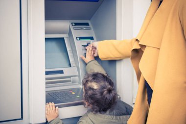 Mother and daughter withdrawing money form cash machine. Small girl assisting her mother with inserting credit card into ATM machine.