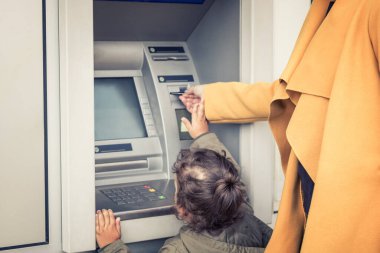 Mother and daughter withdrawing money form cash machine. Small girl assisting her mother with inserting credit card into ATM machine.