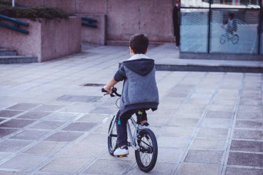 Back view of kid riding a bike in the city.