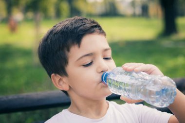 Little boy dringkin fresh water from plastic bottle in the park. 