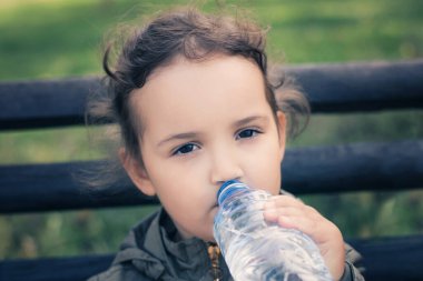 Thirsty girl refreshing herself and drinking water form plastic bottle in the park.  