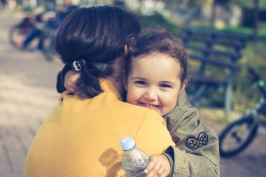 Cute smiling daughter hugging mother and looking at camera. Happy little girl embracing her mother. 