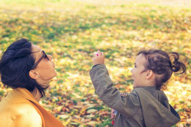Mother and daughter blowing soap bubbles. Happy girl playing with mother and having fun while blowing bubbles in the park. 