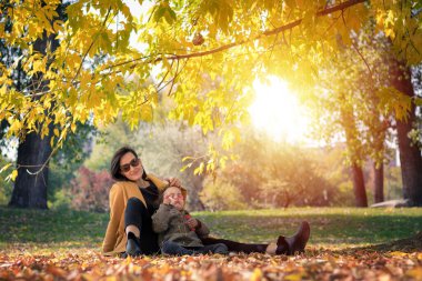 Happy mother enjoying with small daughter in autumn park. Little girl blowing soap bubbles and having fun with her mother in nature.