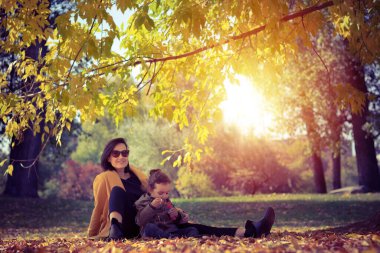Happy mother relaxing in autumn park with her small daughter and spending a day together. 