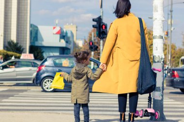 Back view of mother and daughter waiting on zebra crossing and holding hands. 