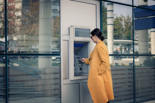 Young woman withdrawing money from ATM machine and inserting credit card at the bank.
