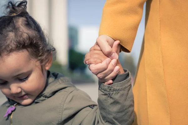 Close up of little girl holding hands with her mother. Mother and daughter bonds. 