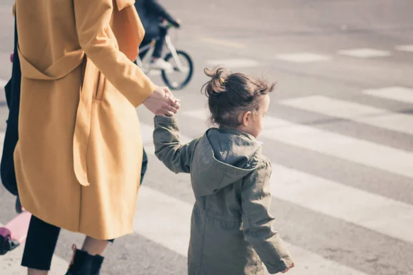 Small girl holding mother's hand on zebra crossing. Mother guiding her daughter while walking a cross the street. 
