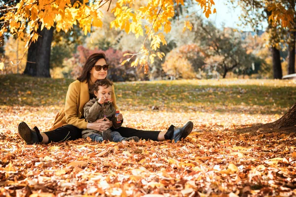 Happy mother and her small daughter relaxing in autumn leaves in nature. 