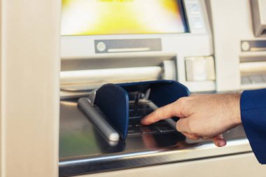 Close-up of man typing pin while withdrawing money at ATM cash machine. 