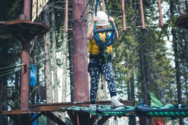 Kid walking over obstacles while being on rope course in the forest. 