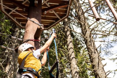 Below view of kid attaching safety harness on zip line during canopy tour in nature.