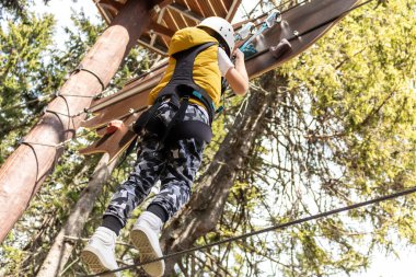 Low angle view of child crossing over hanging rope on canopy tour in nature. 