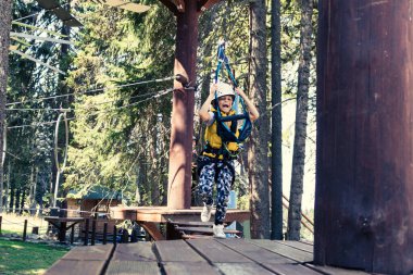 Happy kid running over obstacles and having fun on canopy tour in the forest. 