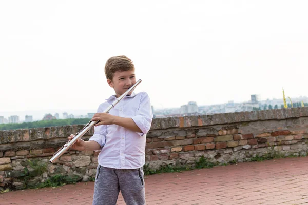 Cute boy playing flute outdoors. 