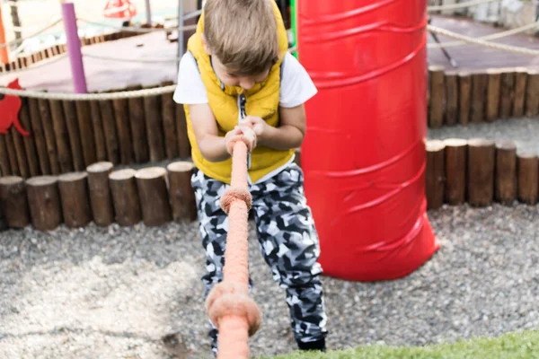 Close up of kid pulling rope while climbing up on the playground.