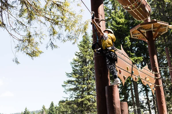 Small boy standing on a platform high up and attaching carabiner on zip line during canopy tour in the forest. 