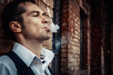 Close-up of serious man smoking while leaning on a wall outdoors. 