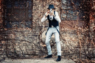 Full length of retro-styled man recording with 8mm video camera outdoors.