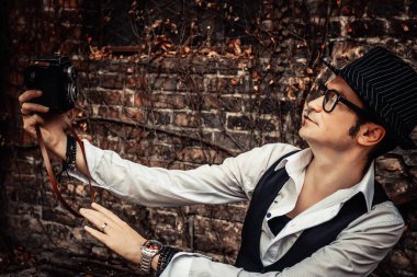 Fedora styled man having fun while taking selfie with medium format camera outdoors. 