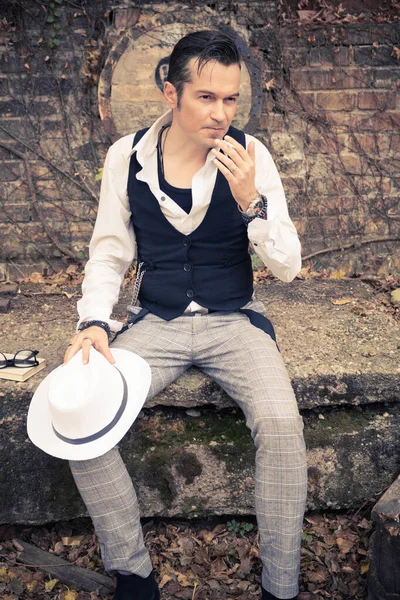 Pensive man with fedora hat smoking cigarette while contemplation outdoors.