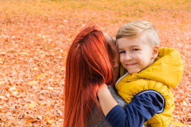 Happy kid embracing his mother during an autumn day at the park. 