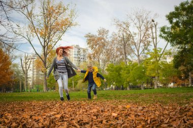 Happy boy holding hands with his mother and running in the park during autumn day.