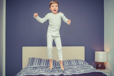 Playful kid in pajamas jumping on the bed and having fun in the morning. 