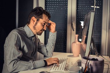 Stressed businessman having headache while working on the computer in the evening at home office. 