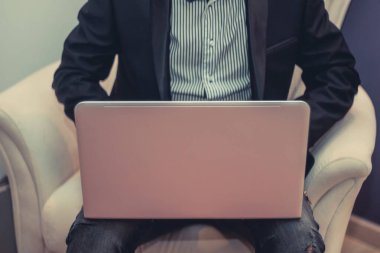 Unrecognizable businessman working on laptop while sitting in armchair.