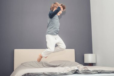Playful boy in pajama jumping high up on the bed and having fun in the evening.