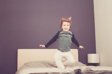 Carefree boy having fun and jumping on the bed at home. 