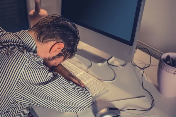 Tired businessman taking a nap at office desk after working on computer in the office.