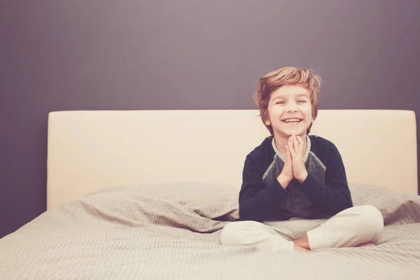 Small boy having fun while sitting in prayer position and doing Yoga exercises in the bedroom. 