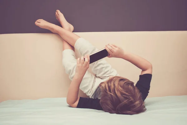 Kid relaxing watching cartoons on the internet while relaxing on the bed. 