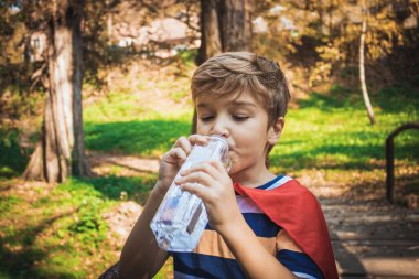 Little boy drinking water while feeling thirsty in nature. 
