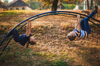 Carefree kids having fun while hanging on monkey bars while playing in the park/ 
